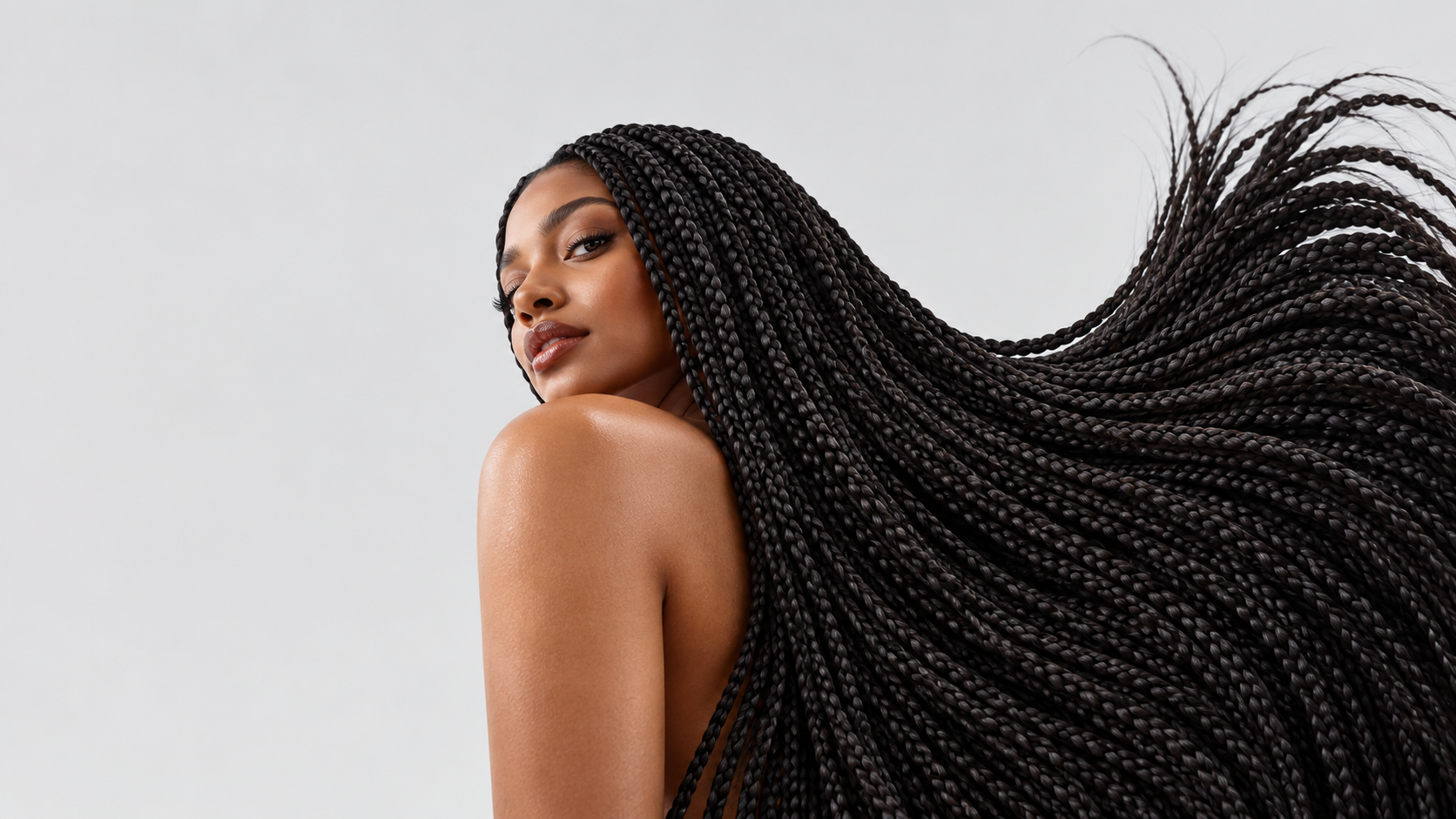 A woman looking over her shoulder as full, long black braids sweep through the air